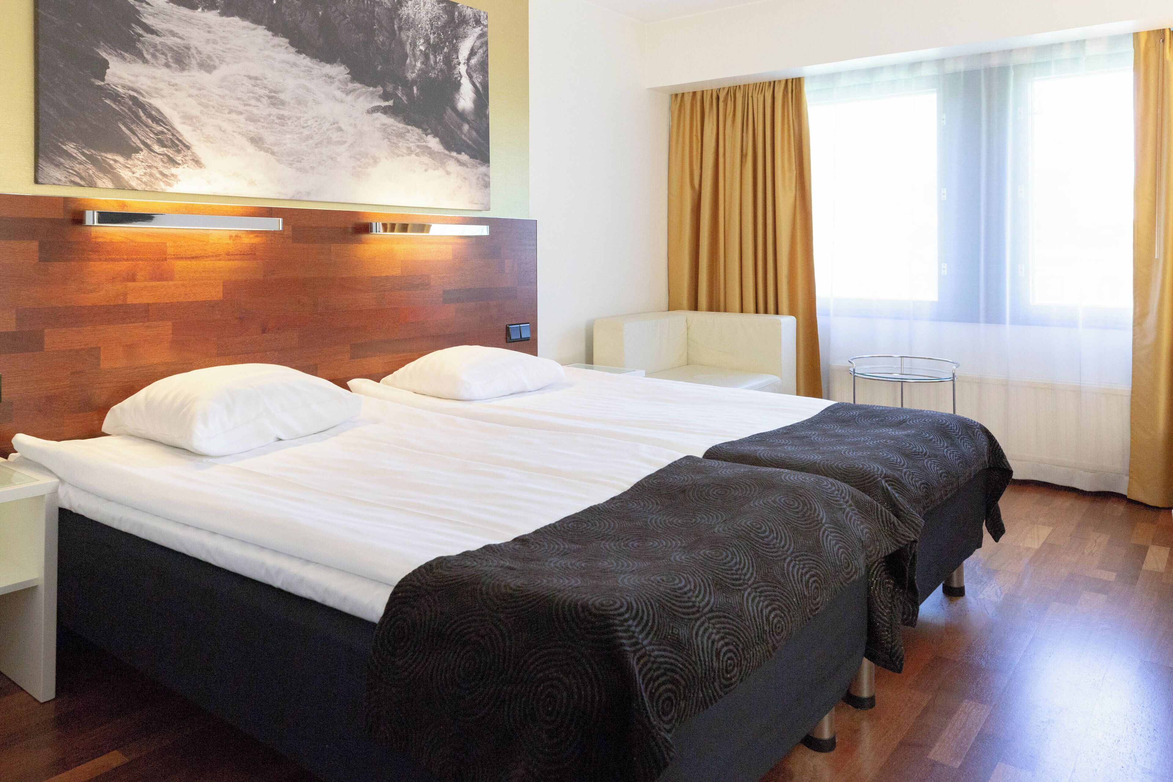 Une chambre d’hôtel avec un grand lit, des tables de chevet, une chaise, une petite table et une fenêtre avec des rideaux.