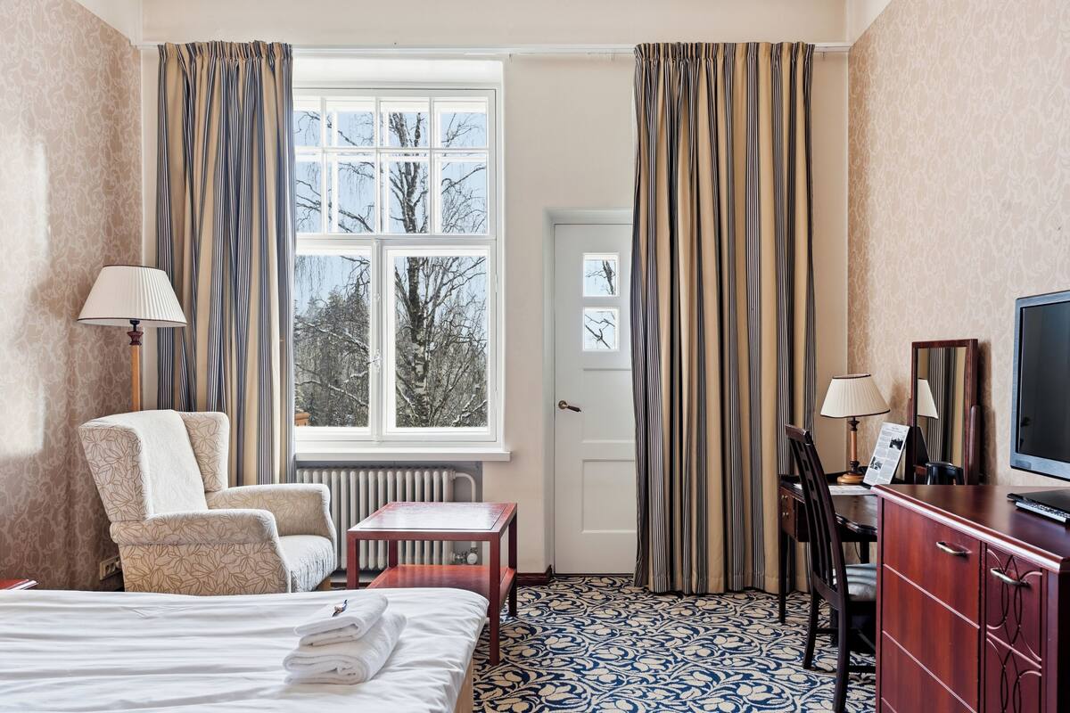 A hotel room with a bed, a chair, a desk, a television, and a window with curtains.