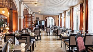 Een restaurant met houten vloeren, tafels gedekt met glazen en een hoog plafond met zichtbare balken.