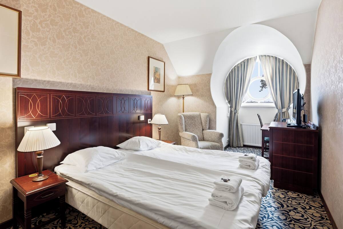 A hotel room with a large bed, a chair, a desk, and a window with curtains.