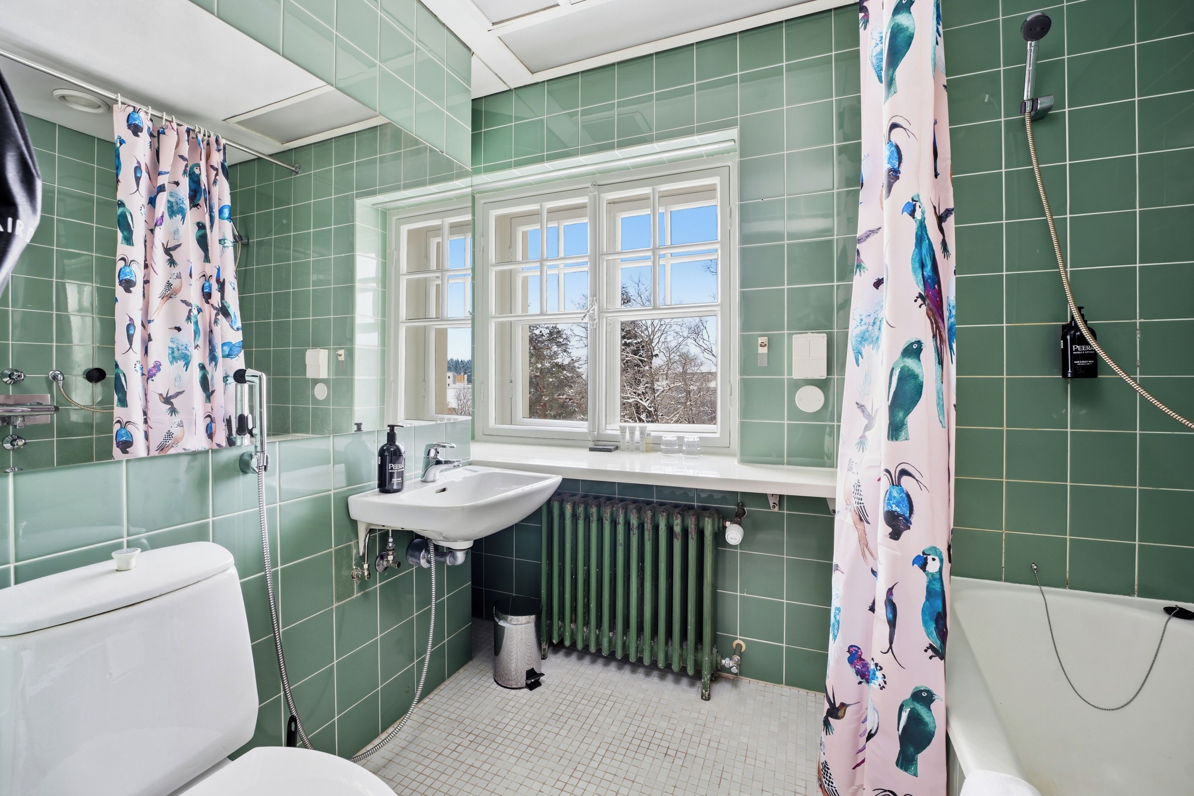 Une salle de bain avec des carreaux verts, une fenêtre, un lavabo, des toilettes et une douche.