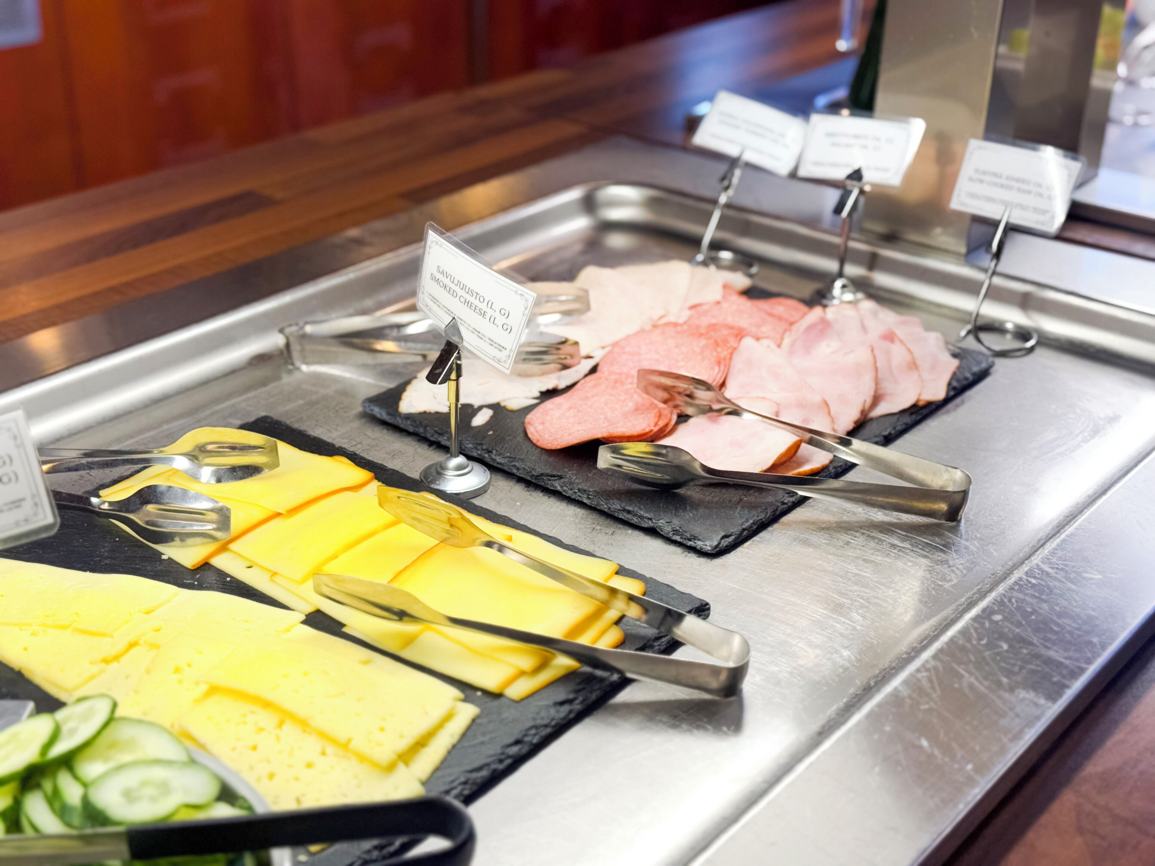 A buffet with various cheeses, meats, and sliced cucumbers.