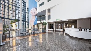 Een ruime lobby met een hoge plafond, een receptiebalie en een groot muurschilderij.