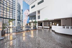 Um hall amplo com teto alto, balcão de recepção e um grande mural na parede.