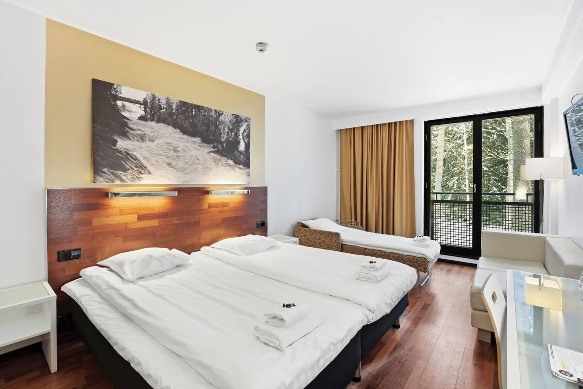 A hotel room with two beds, a desk, a chair, a large window with a view, and a wall-mounted artwork.