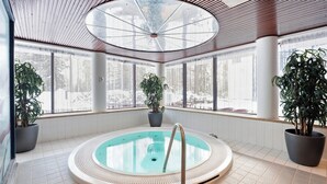 Een wellnessruimte met een rond bubbelbad, grote ramen en potplanten.
