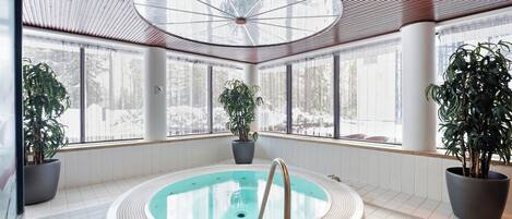 A spa area with a circular hot tub, large windows, and potted plants.