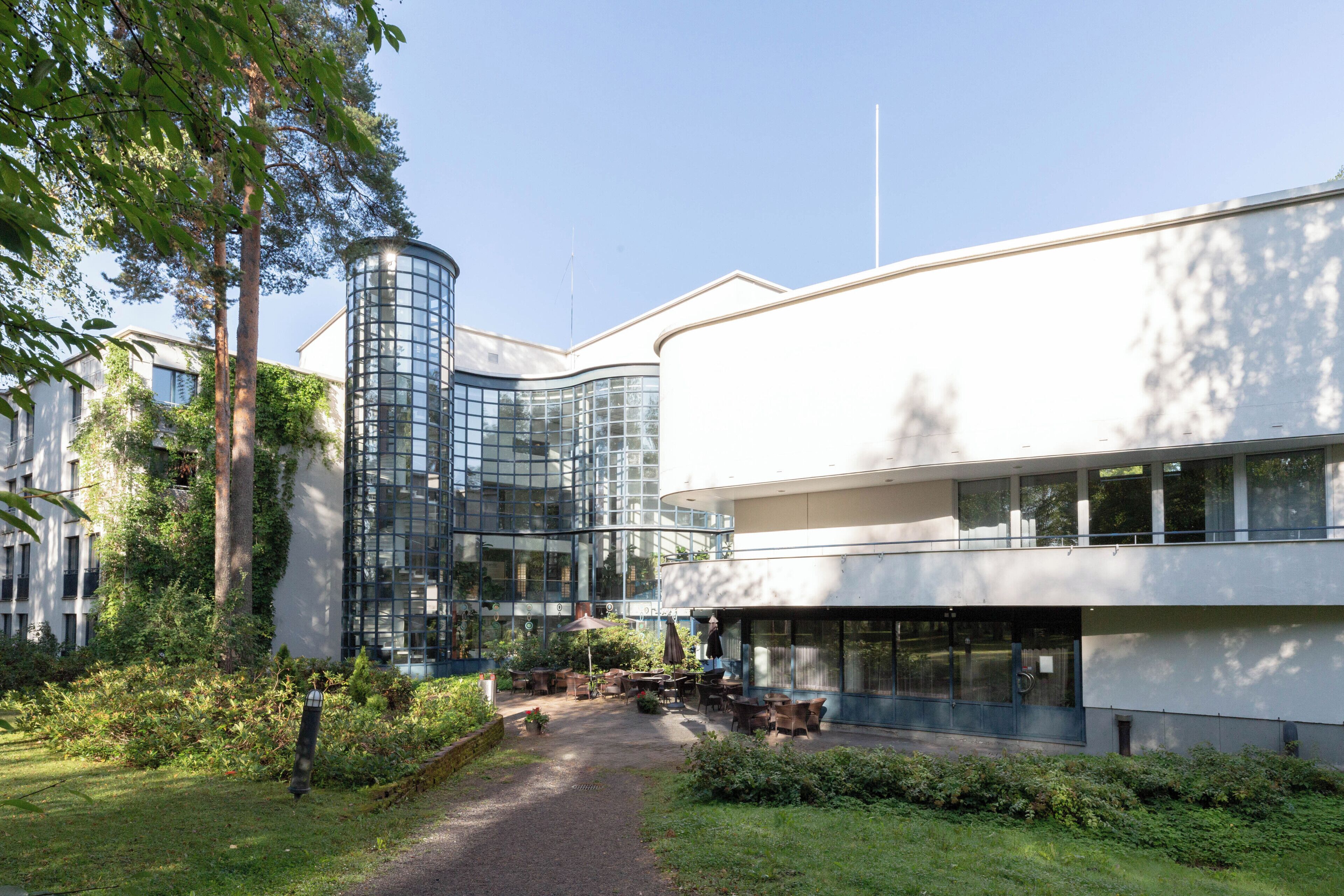 A modern building with a glass facade, surrounded by greenery and a paved pathway.
