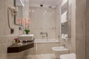 A modern bathroom with a large mirror, a bathtub, a bidet, and a vanity with a sink and decorative items.