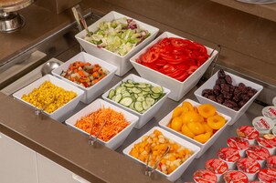 A buffet with various food items including corn, carrots, cucumbers, tomatoes, and dates.