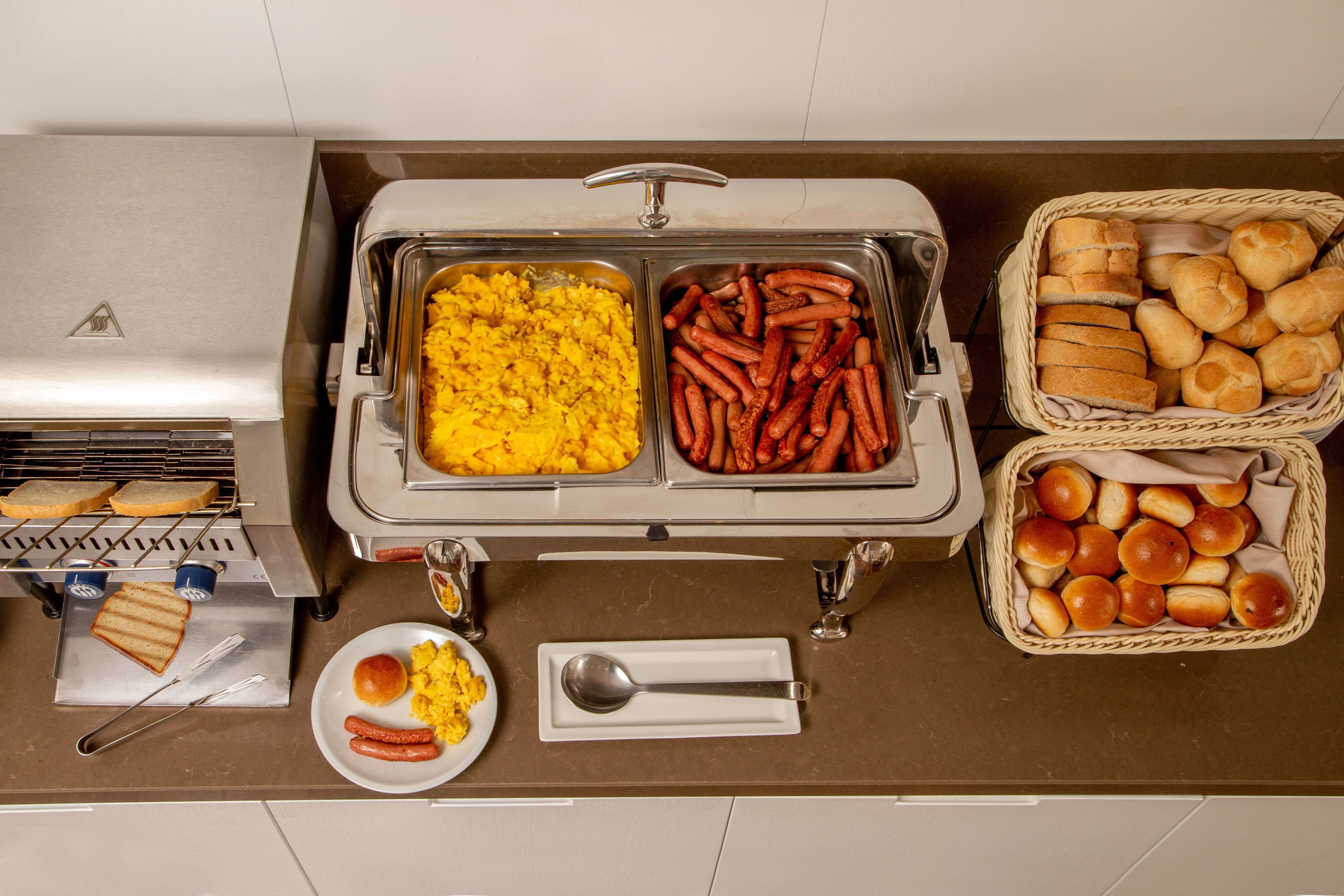 A buffet setup with various food items including scrambled eggs, sausages, and rolls.