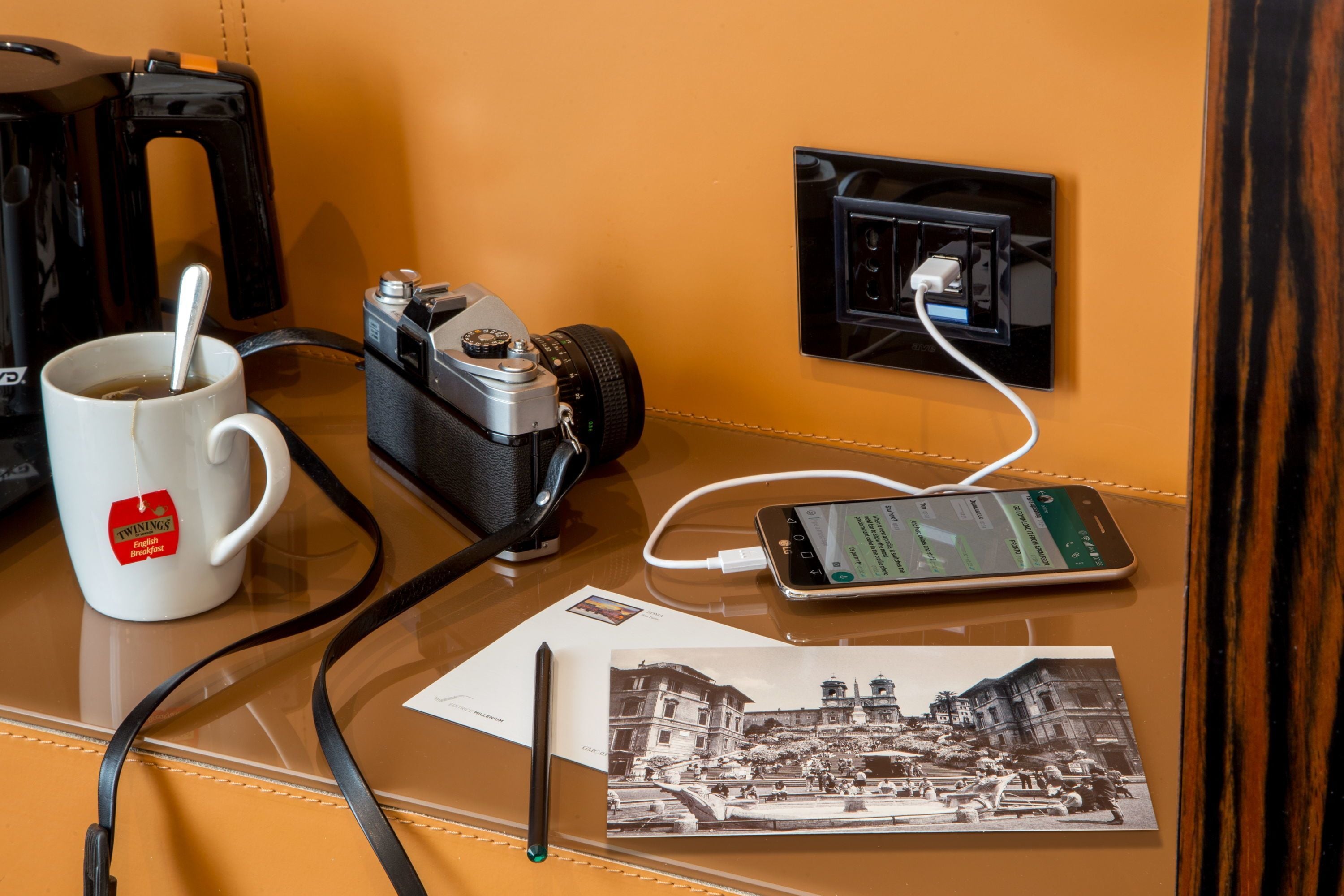 A coffee mug, a camera, a smartphone, and a postcard on a table.