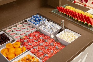 Een buffet met diverse etenswaren, waaronder Yomo yoghurt, fruit en een watermeloenpresentatie.