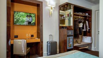 A hotel room with a bed, a desk with a chair, a mirror, a wardrobe, and a television.