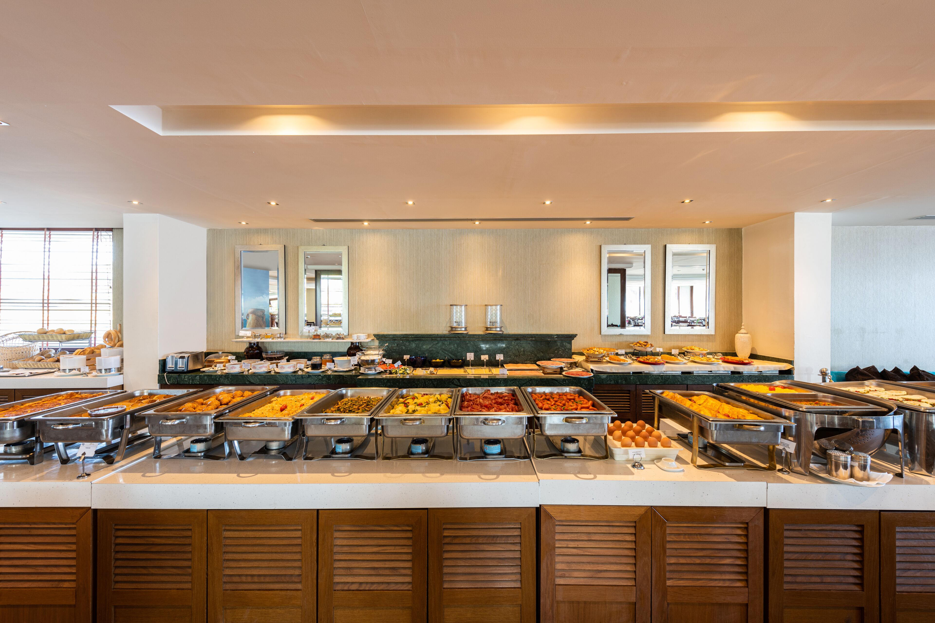 Buffet com diversas opções de comida, bancada de mármore e armários de madeira.