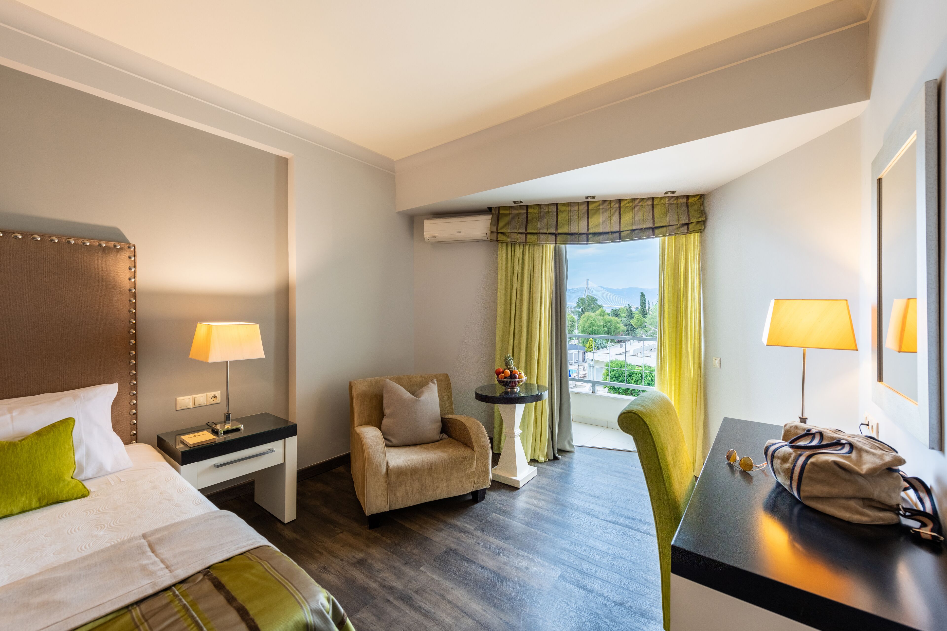 A hotel room with a bed, a chair, a desk, and a view of a cityscape.