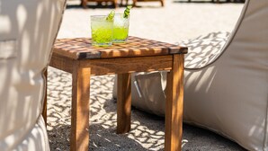 Eine Strandlounge mit Tisch und zwei Gläsern eines grünen Getränks, umgeben von Liegestühlen und Strohsonnenschirmen.