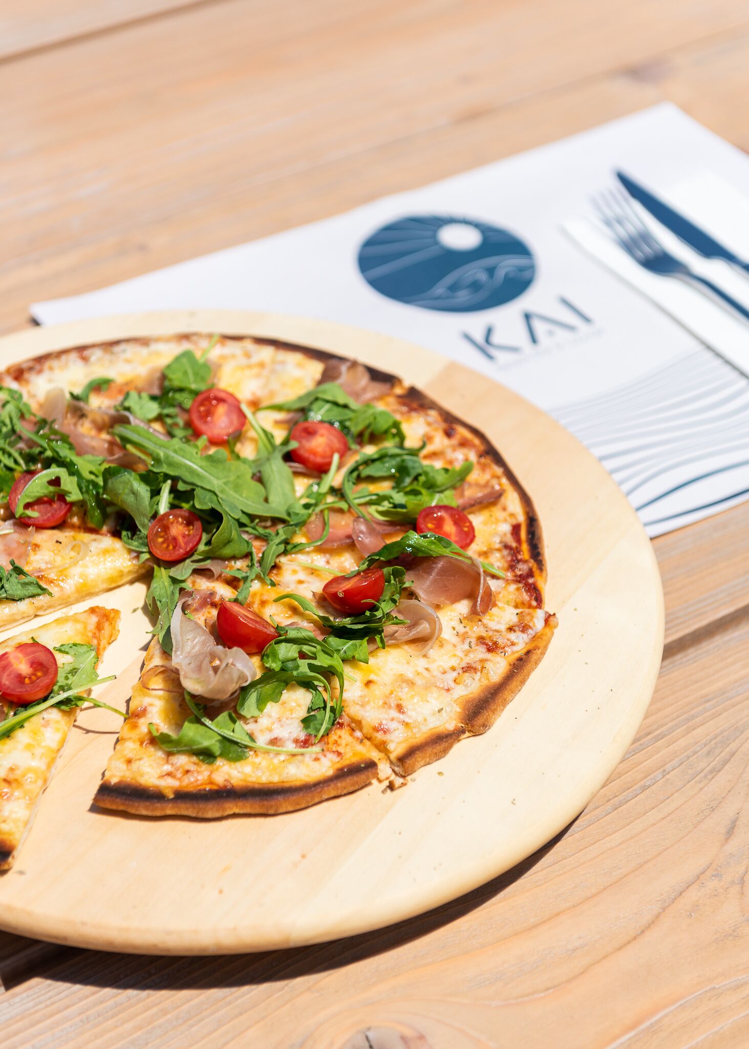Pizza puulautalla, sen vieressä servetti ja ruokailuvälineet.