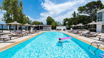 A swimming pool with lounge chairs and umbrellas, surrounded by trees and a clear sky.