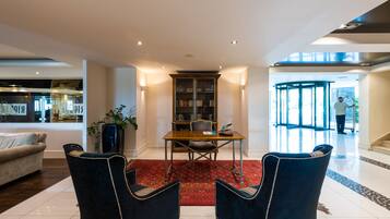 A modern living room with a dining area, featuring a red rug, two blue chairs, a wooden table, and a bookshelf.