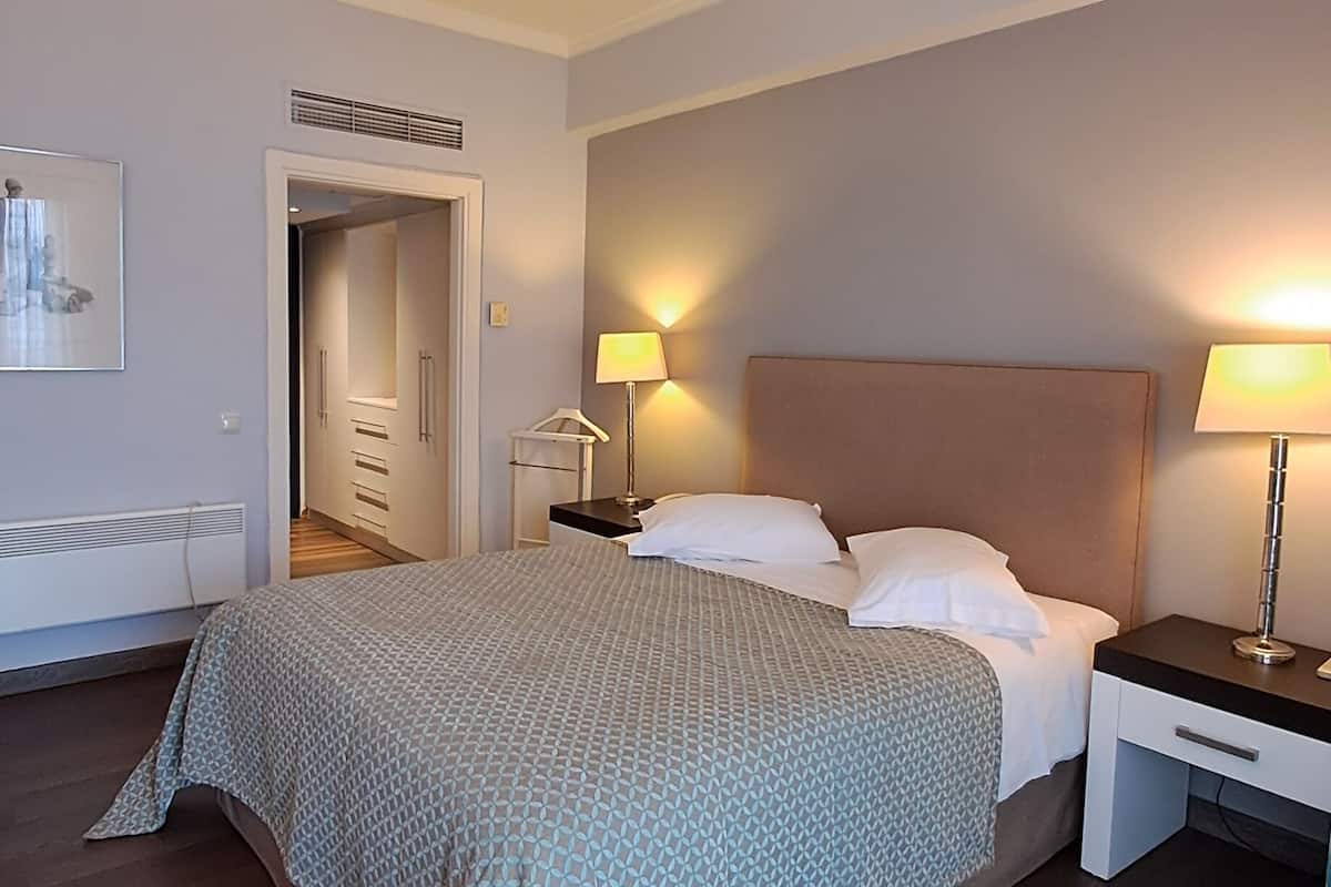 A hotel room with a large bed, two bedside tables with lamps, a wardrobe, and a door leading to a hallway.