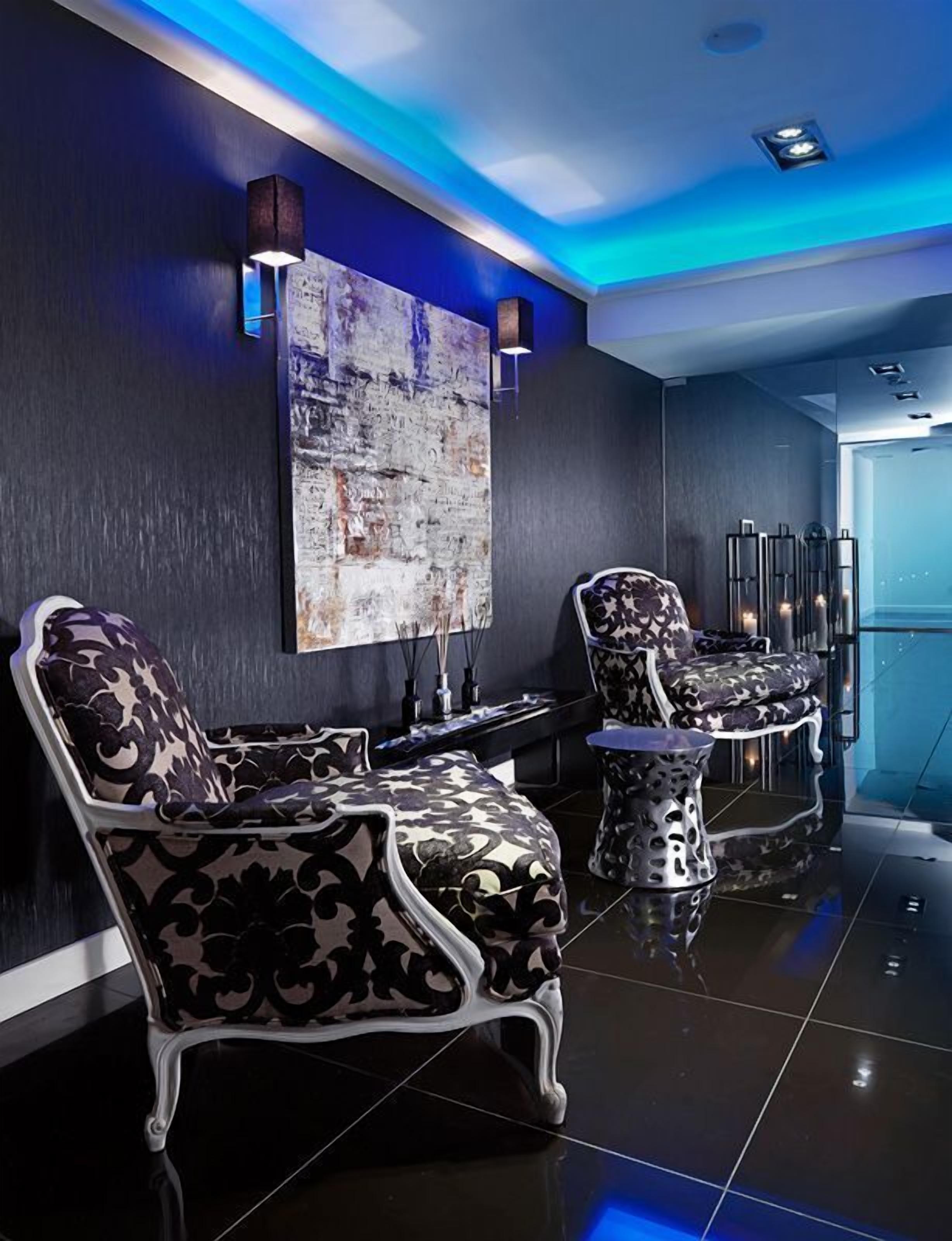 A modern lounge with black and white patterned chairs, a large abstract painting, and ambient blue lighting.