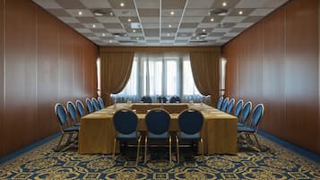 Een vergaderruimte met een lange tafel, blauwe stoelen en een kamerbreed tapijt met een patroon.