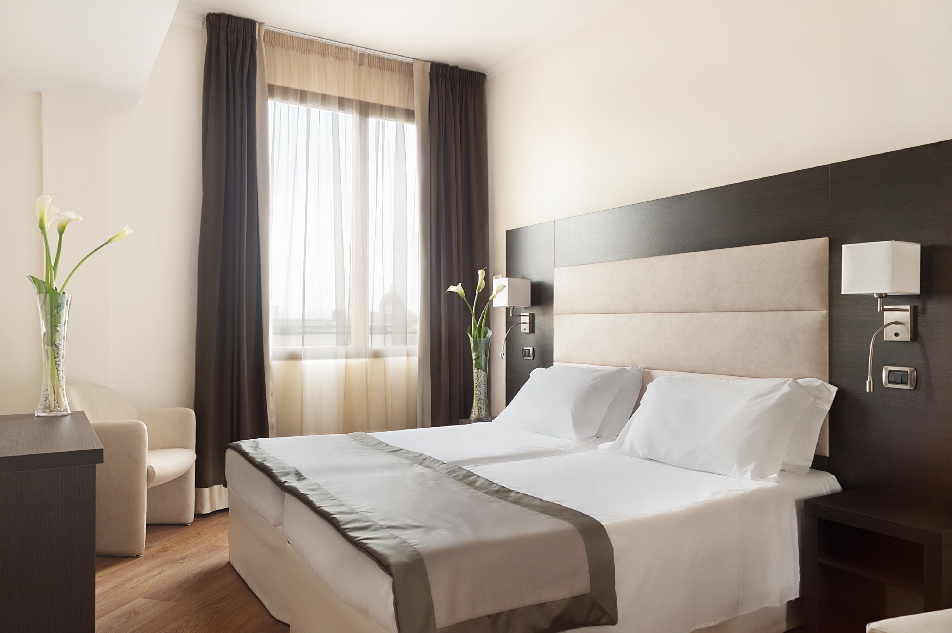 Ein Hotelzimmer mit einem großen Bett, Nachttischlampen, einem Nachttisch, einem Schreibtisch und einem Stuhl.