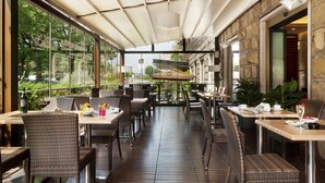 A covered outdoor dining area with wicker furniture and a stone wall backdrop.