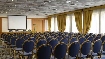 A conference room with rows of blue chairs, a podium, and a projector screen.