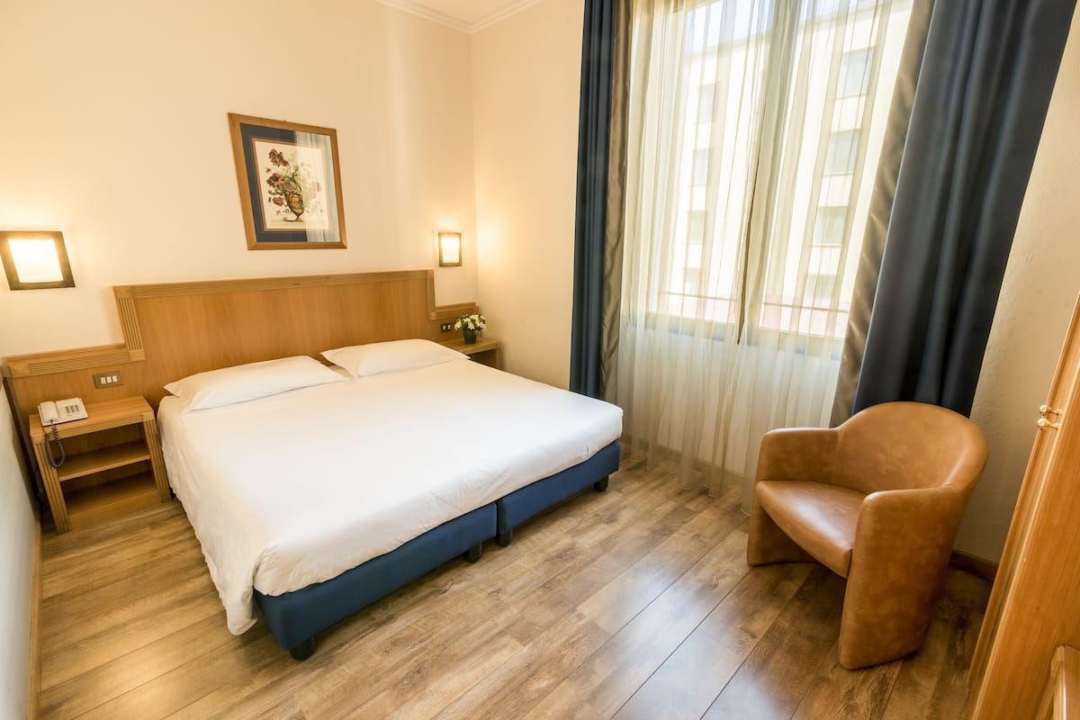 Une chambre d’hôtel avec un lit, des tables de chevet, une chaise et une fenêtre avec des rideaux.