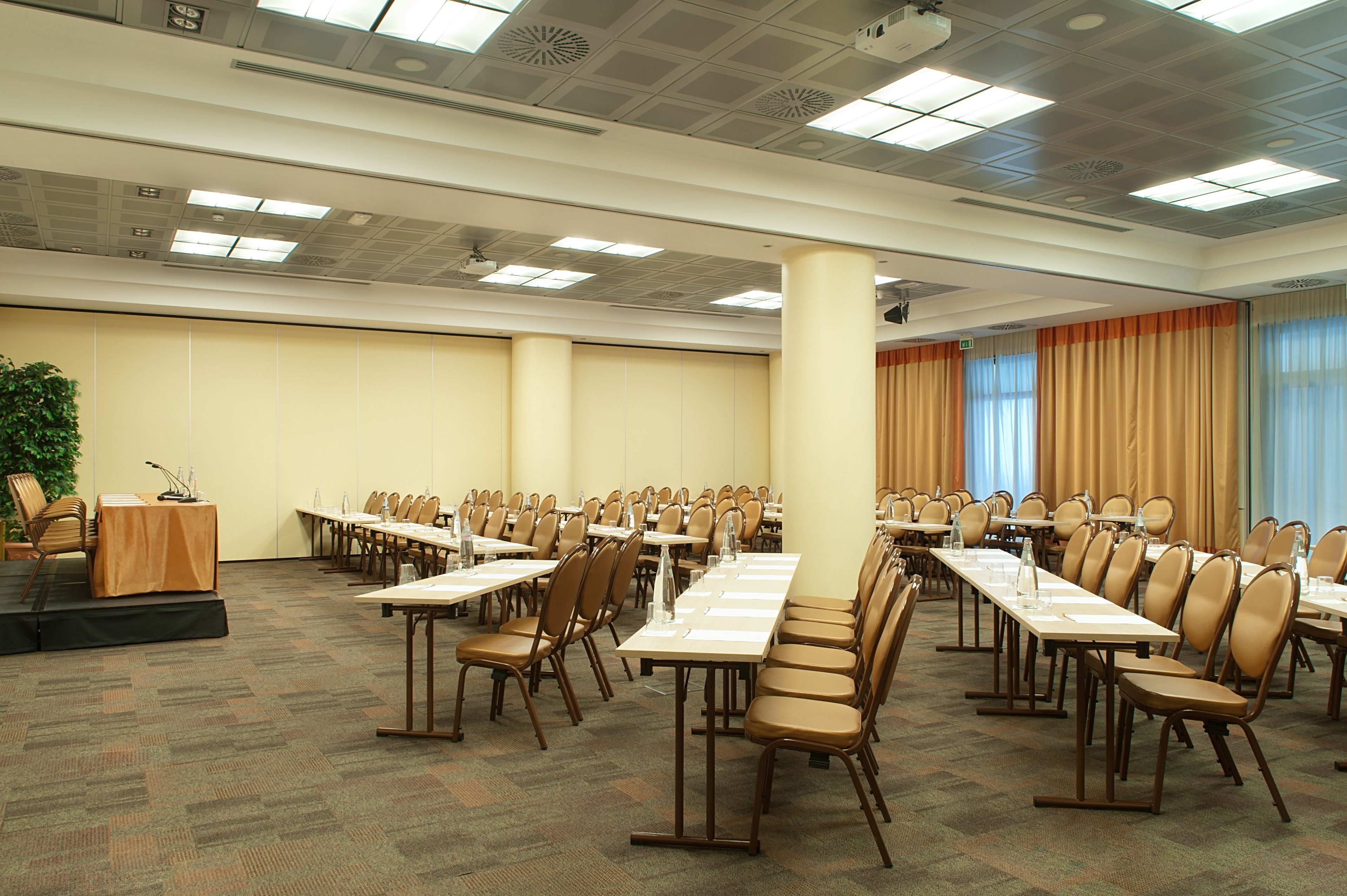 Un salón de conferencias con varias mesas y sillas, un atril y una planta.