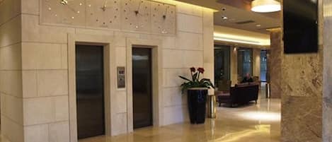 A lobby with a reception desk, two elevators, and a marble column.