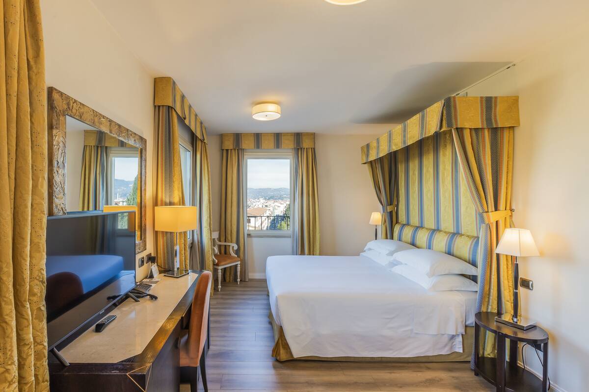 Une chambre d’hôtel équipée d’un lit, d’un bureau, d’une chaise, d’une télévision et offrant une vue sur la ville par la fenêtre.