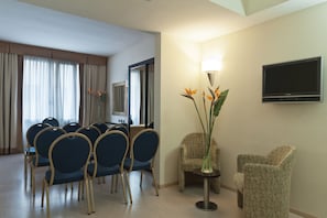 A hotel room with a dining area, a TV mounted on the wall, and a table with chairs.