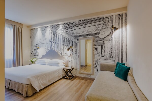 A hotel room with a large bed, a smaller sofa, and a wall with a black and white mural.