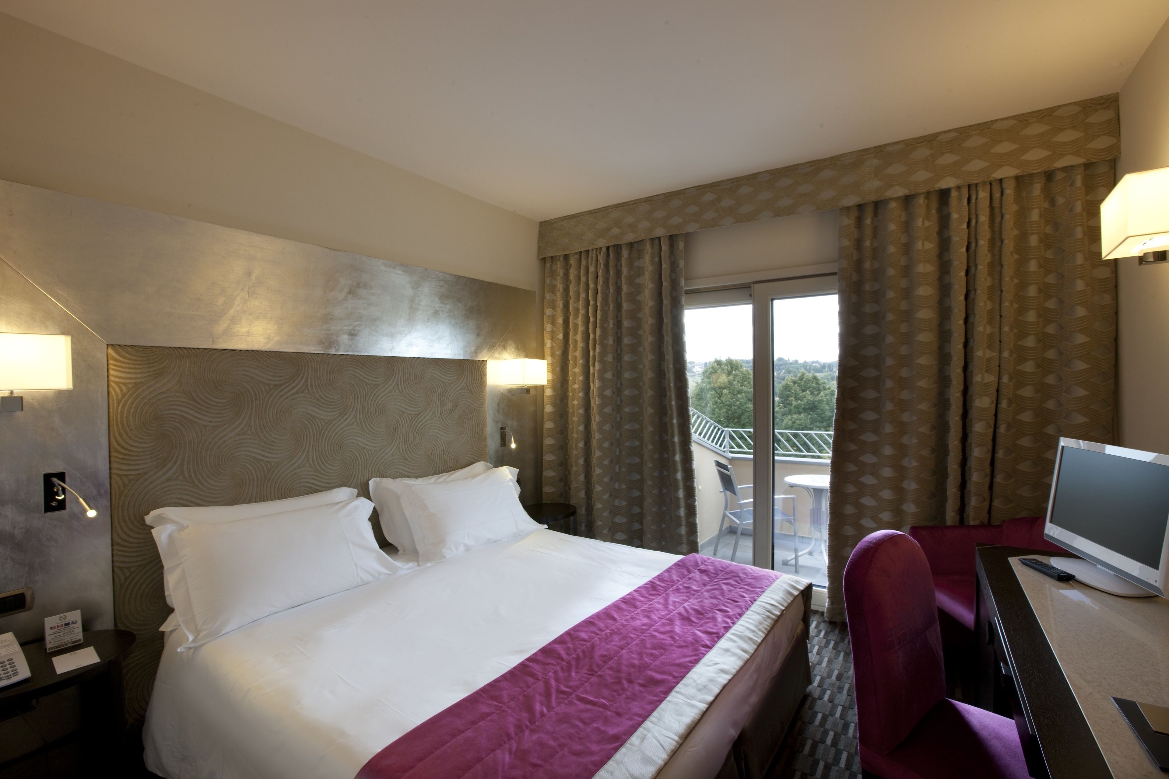 Ein Hotelzimmer mit einem großen Bett, einem Schreibtisch mit Computer und Blick ins Freie.