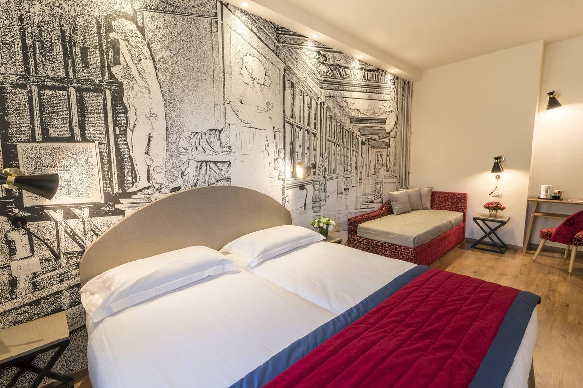 Une chambre d’hôtel avec un grand lit, un petit canapé, un bureau et une fresque murale.