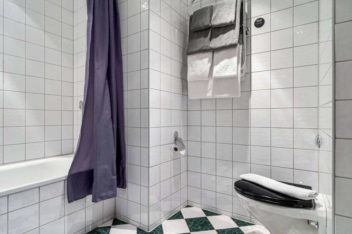 Ein Badezimmer mit weiß gefliesten Wänden, einem Schachbrettfußboden, einer Badewanne und einem WC mit Handtuch.