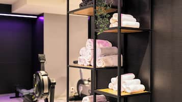 A neatly organized shelf with towels in various colors, a hanging plant, and exercise equipment in the background.
