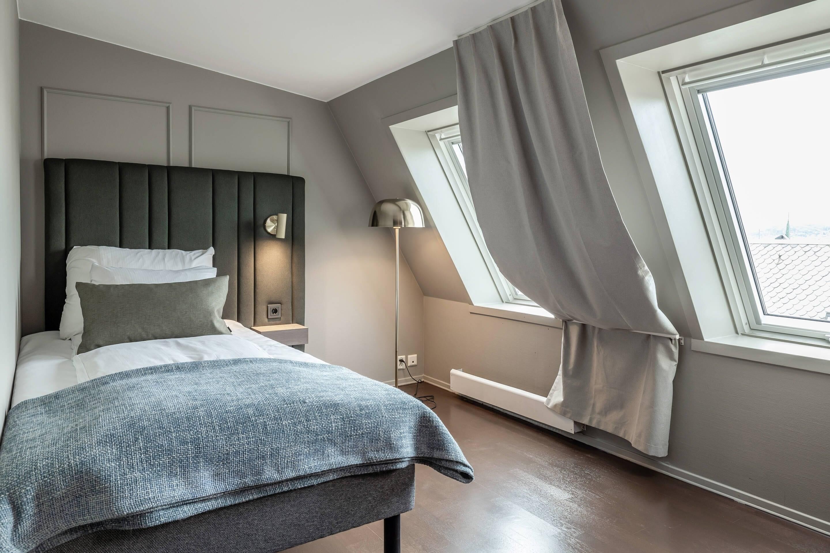 A modern bedroom with a bed, a nightstand, a lamp, and a window with curtains.