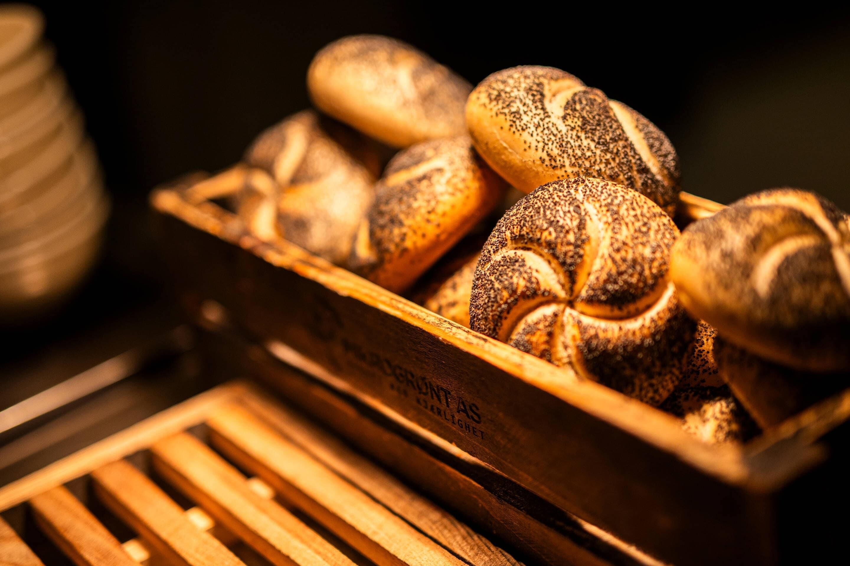 A wooden crate filled with various types of bread, including poppy seed and sesame seed varieties.