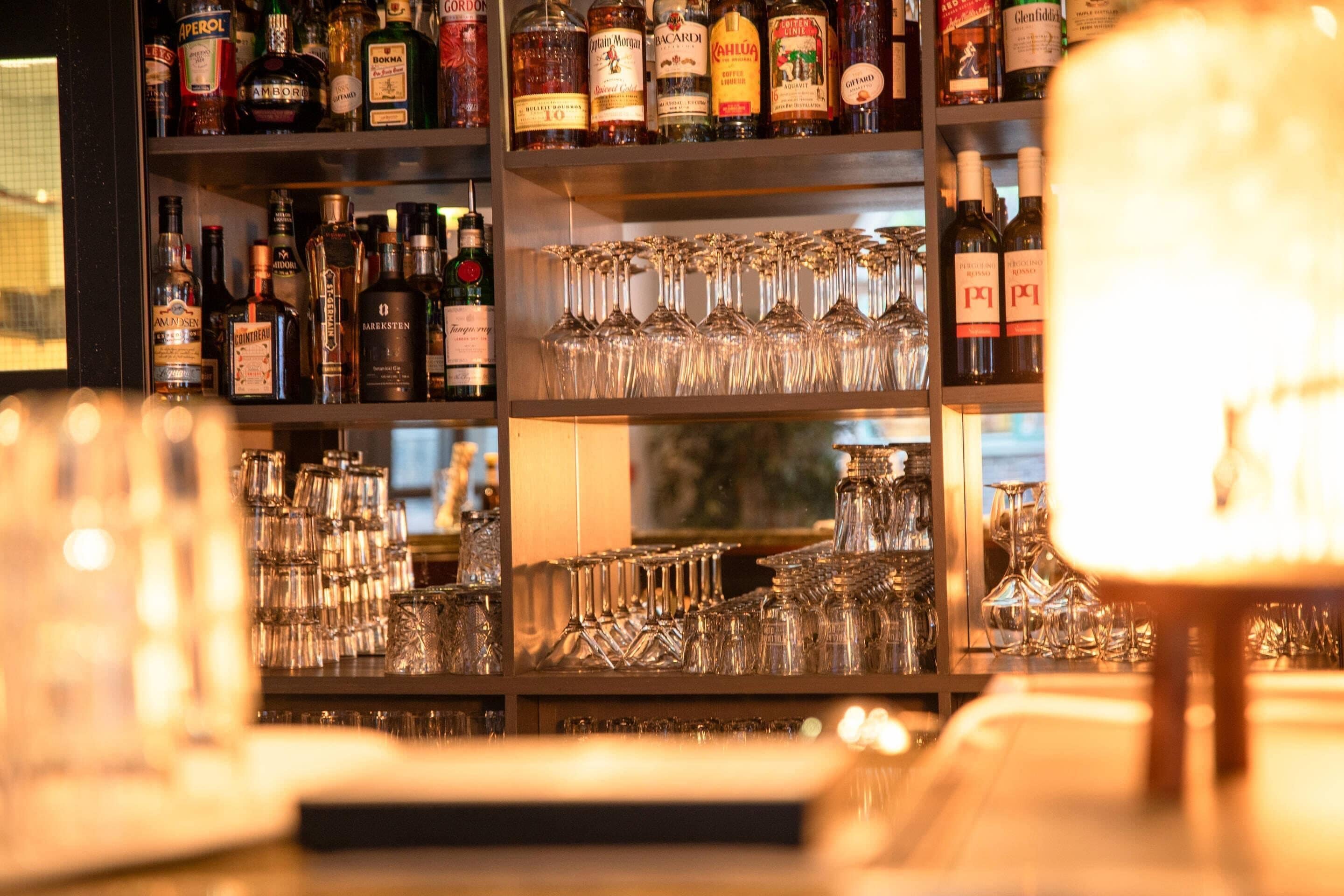 A bar area with shelves of liquor bottles and a collection of wine glasses.