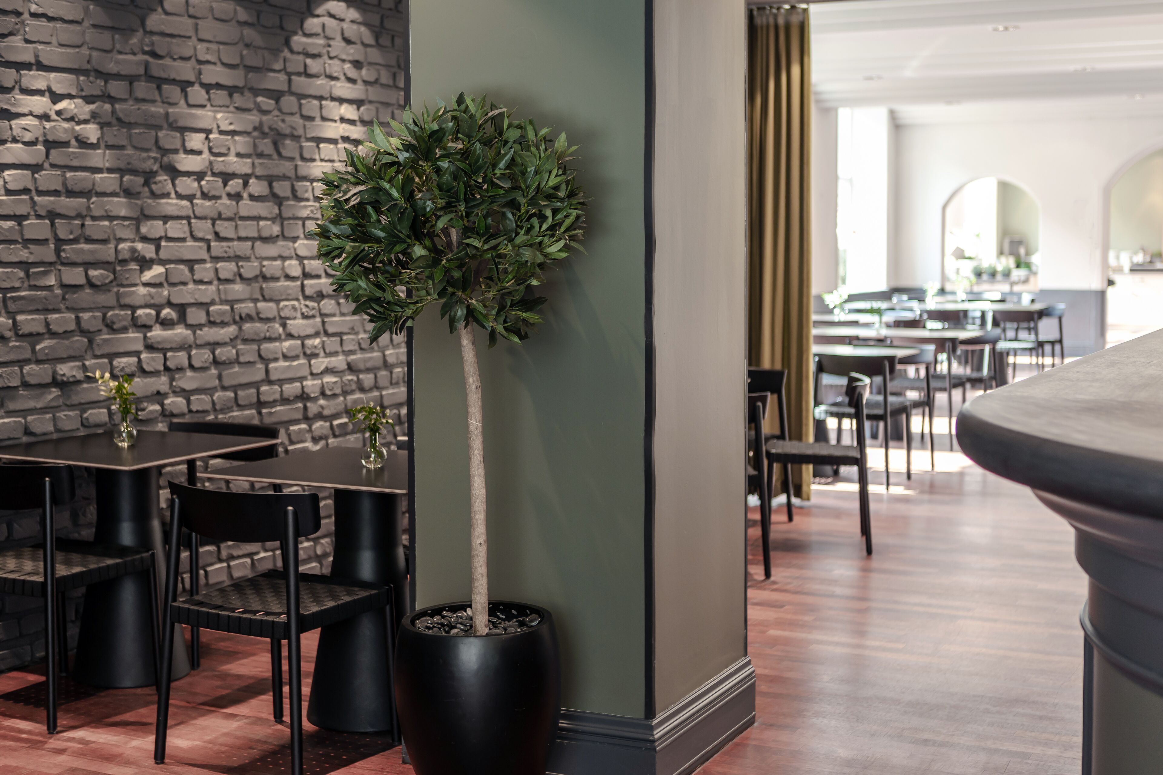 Un intérieur moderne avec un mur en briques, un arbre en pot et un coin repas avec des chaises et des tables noires.