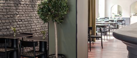 A modern interior with a brick wall, a potted tree, and a dining area with black chairs and tables.