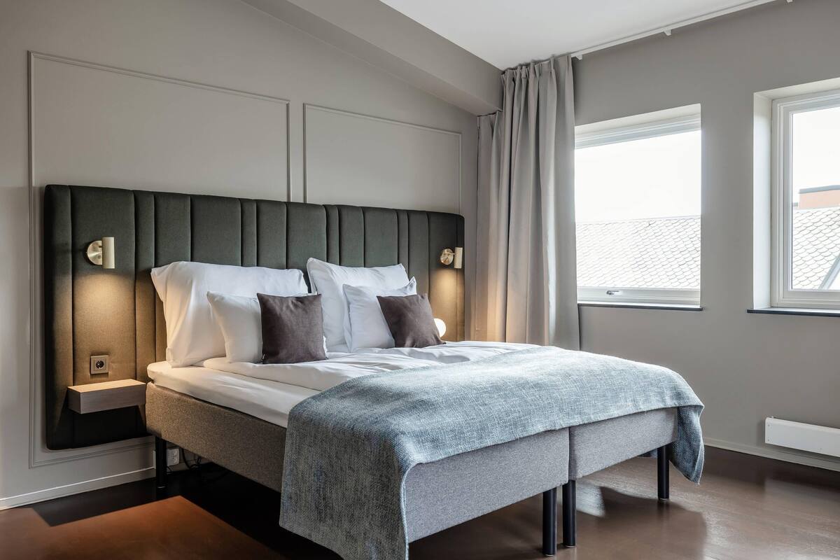 Ein modernes Schlafzimmer mit einem großen Bett, Nachttischen und Blick durch ein Fenster nach draußen.