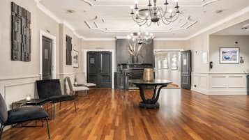 A spacious lobby with a wooden floor, black upholstered chairs, a chandelier, and a fireplace.