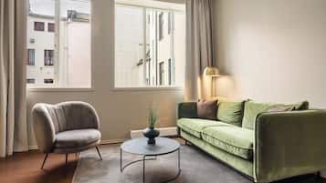Uma sala de estar com um sofá verde, uma poltrona cinzenta, uma mesa de centro redonda e um abajur.
