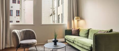 Ein Wohnzimmer mit einem grünen Sofa, einem grauen Sessel, einem runden Couchtisch und einer Stehlampe.