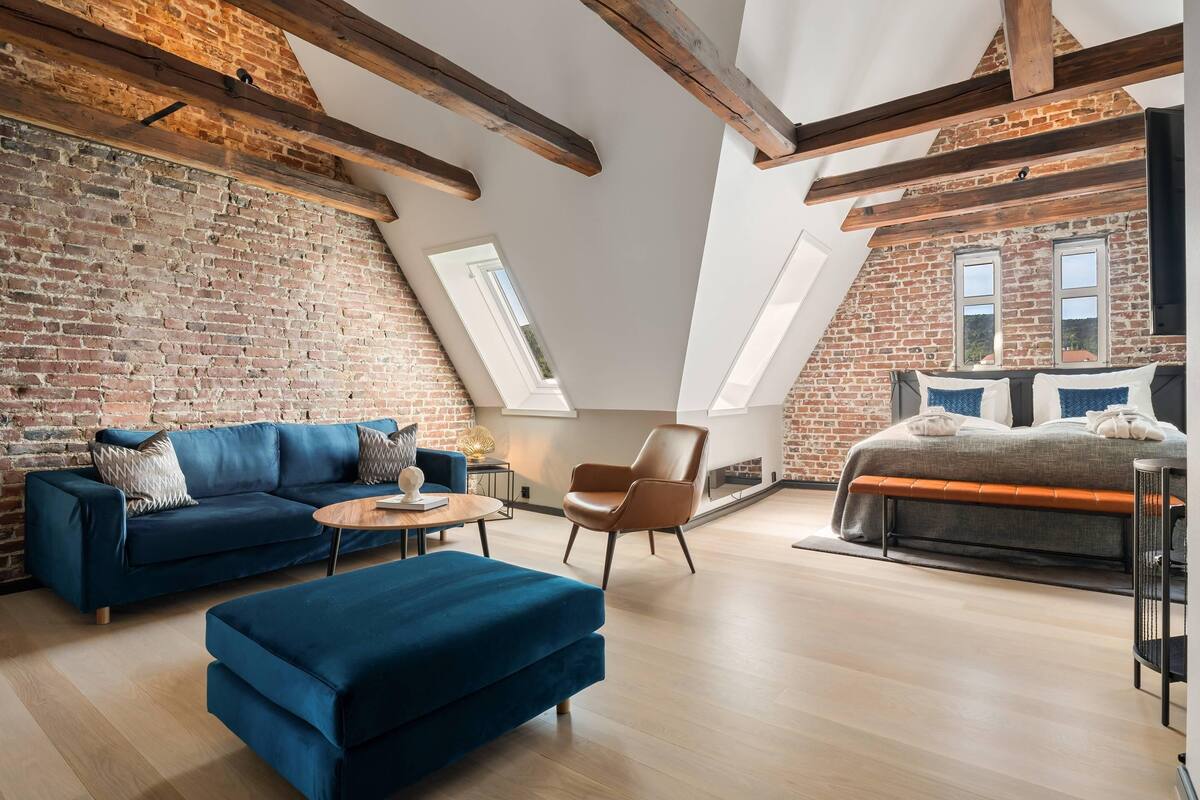 Ein Schlafzimmer im Loft-Stil mit freiliegenden Holzbalken, einer Ziegelwand, einem Schlafplatz in der Höhe und einem großen Fenster.